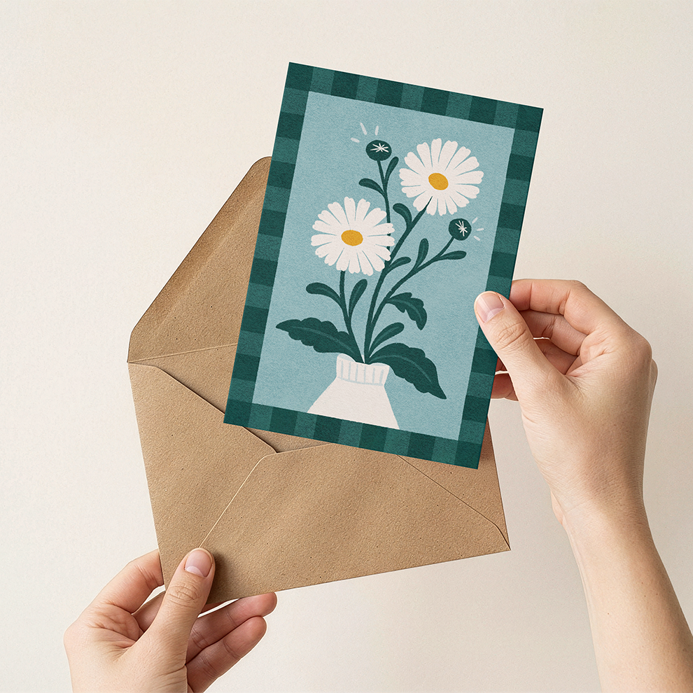 Hand holding a card with floral design and an envelope on a beige background