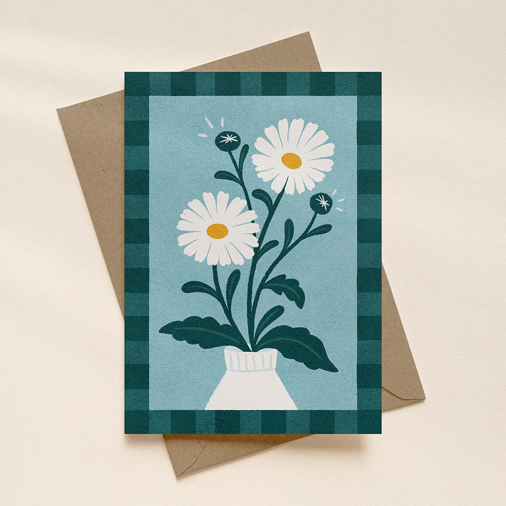 Greeting card with daisy design on a checkered border, placed on a beige surface.