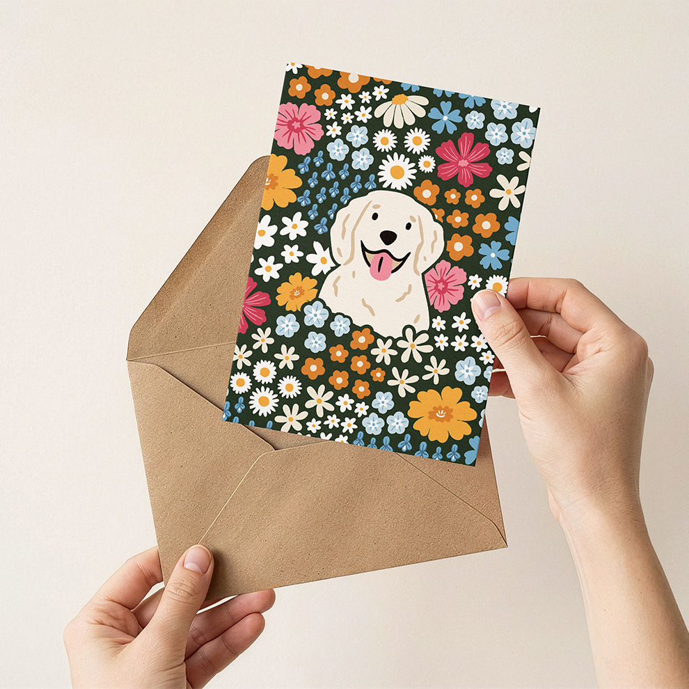Hand holding a card with a dog illustration and floral design, placed on a brown envelope.