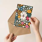 Greeting card with a dog illustration on a floral background held over an envelope.