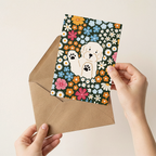 Greeting card with a dog illustration and flowers held over a brown envelope.