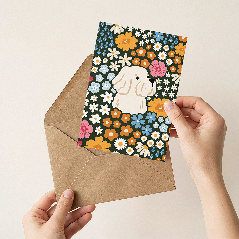 Floral card with a dog design held over a brown envelope against a beige background
