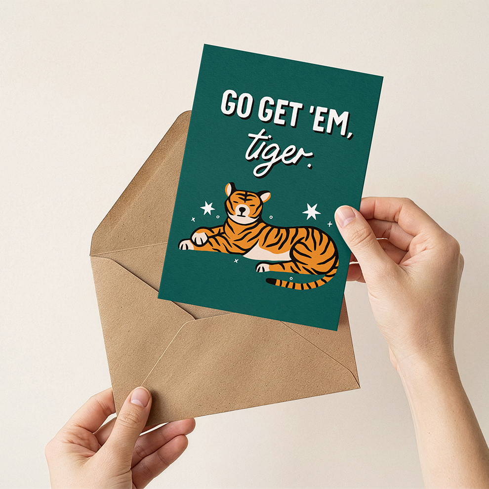 Hand holding a card with a tiger illustration and text 'GO GET 'EM, tiger' over an envelope.