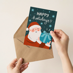 Hand holding a Christmas card with Santa Claus and 'Happy holidays!' text, placed on an open envelope.