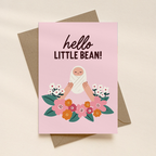 Greeting card with illustration of a baby and flowers, text 'hello little bean!', on a pink background.