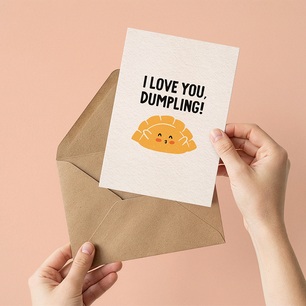 Card with 'I Love You, Dumpling!' text held over a brown envelope against a pink background