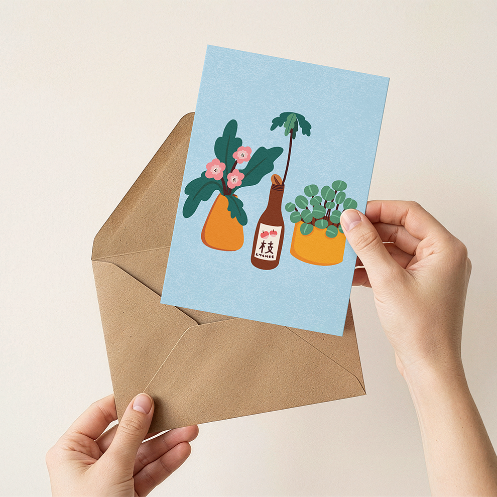 Hand holding a card with plant illustrations and an envelope on a beige background