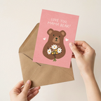 Card with bear illustration and 'Love you, mama bear!' text held over a brown envelope.