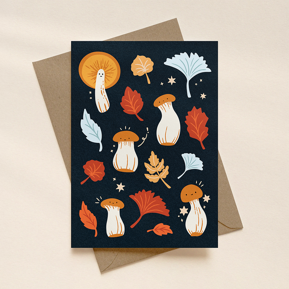 Greeting card with autumn-themed illustrations of mushrooms and leaves on a dark blue background, placed on a beige surface.